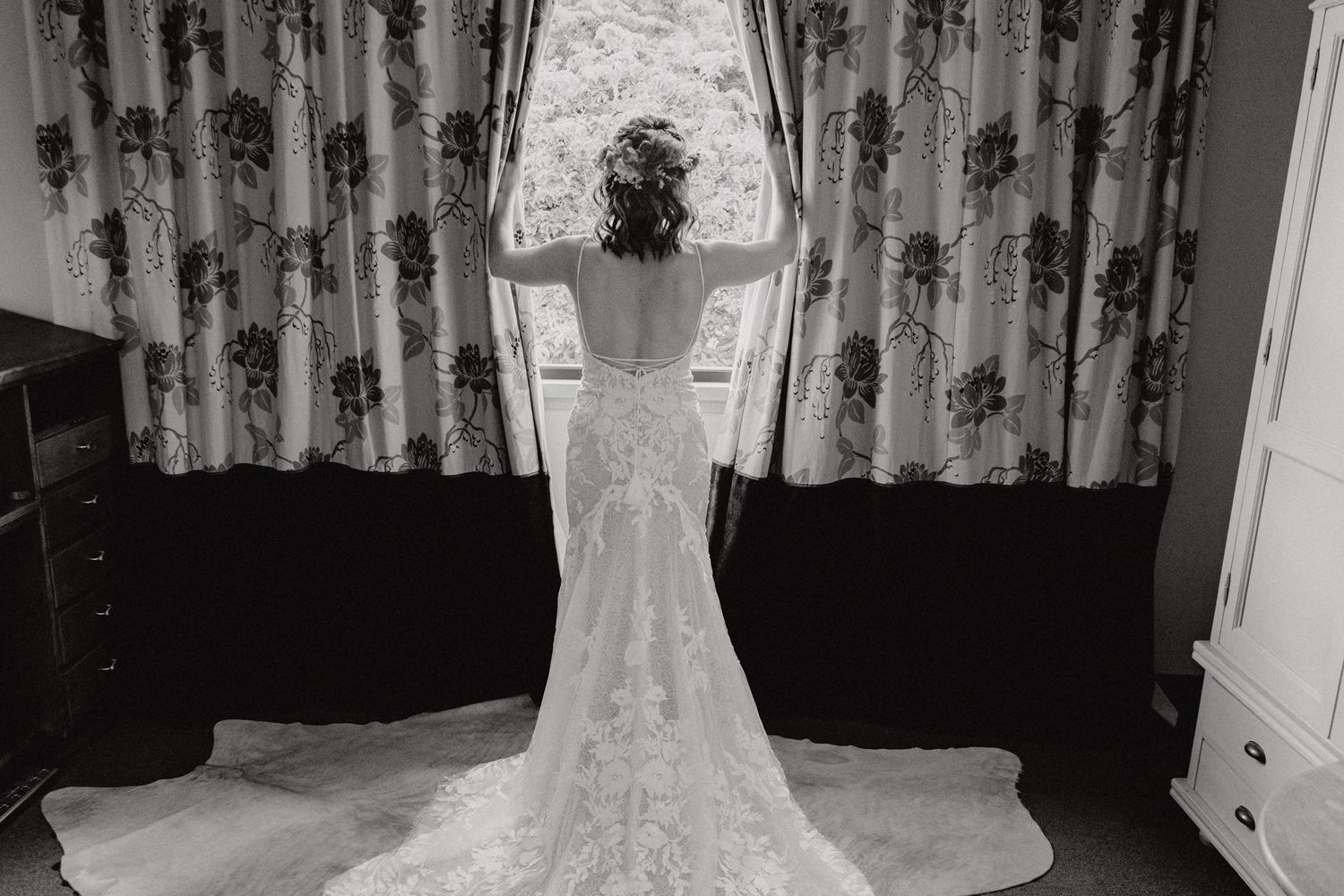 Back view of a lace wedding gown with train against floral curtains in black and white.