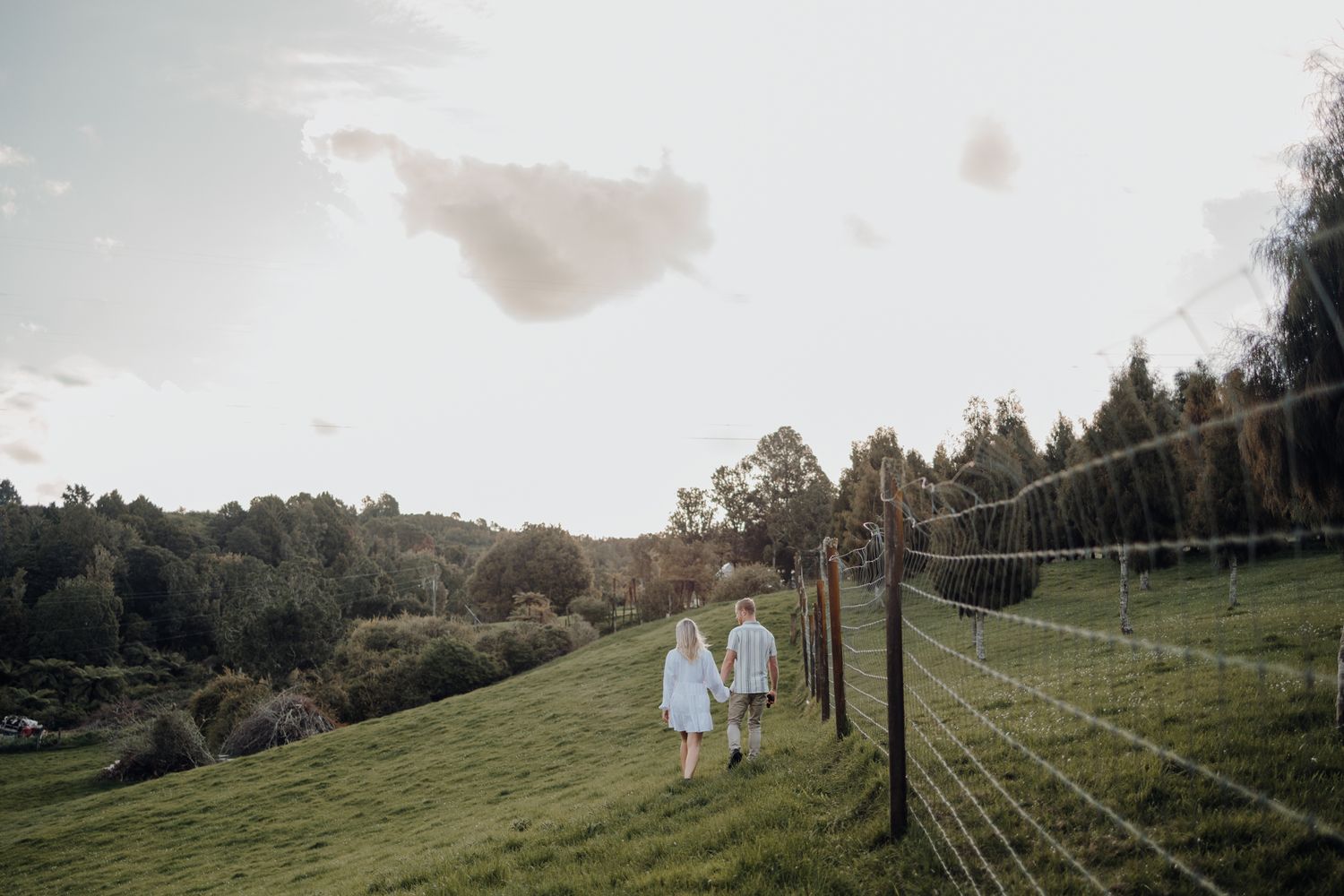 Couple walks hand in hand along a fenced path during golden hour.