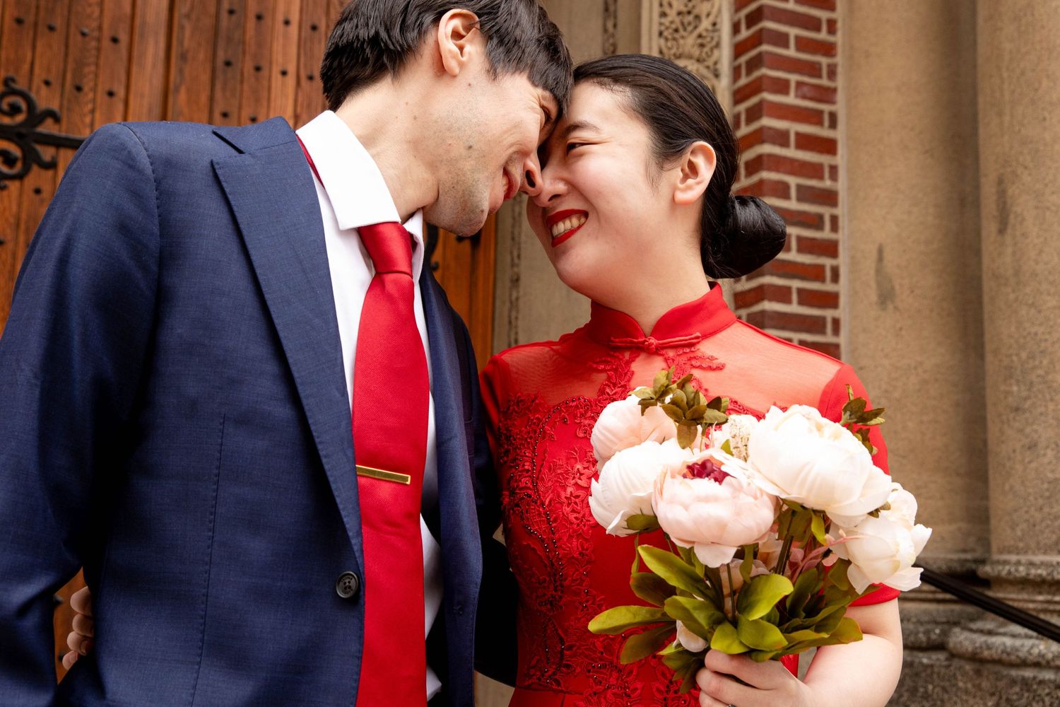 A couple shares a joyful moment with a bouquet of pink and white flowers.