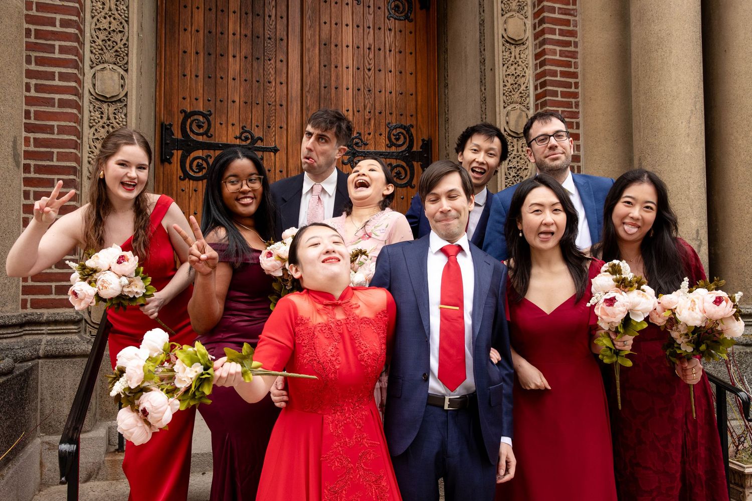 Wedding party laughs together during candid moment in front of brick church entrance.