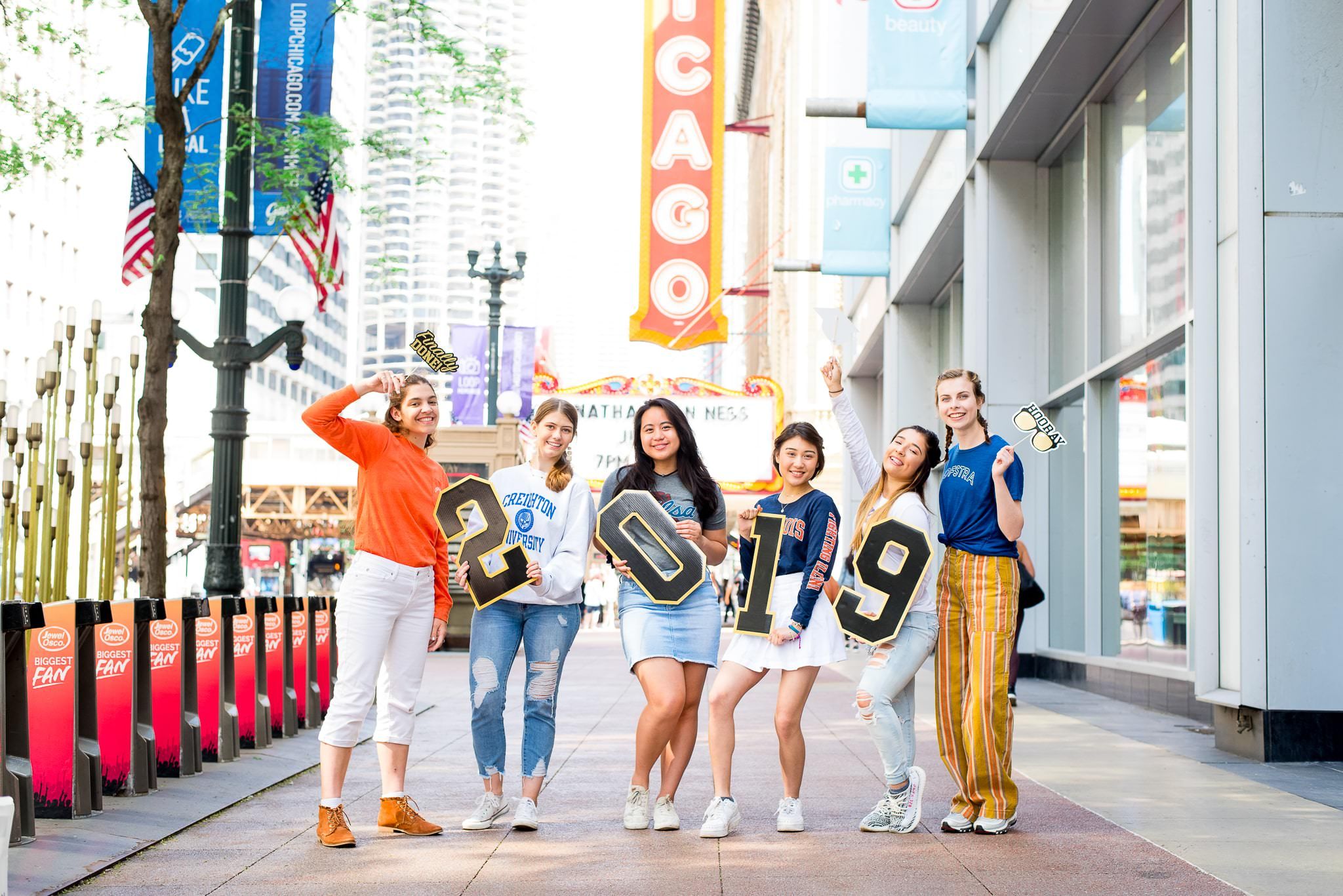 six senior girls in front of the Chicago Theater sign for Chicago senior pictures holding up 2019