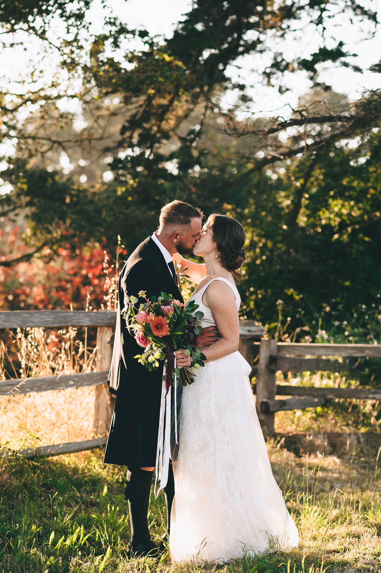 Bride and groom sharing a kiss in a golden field at sunset