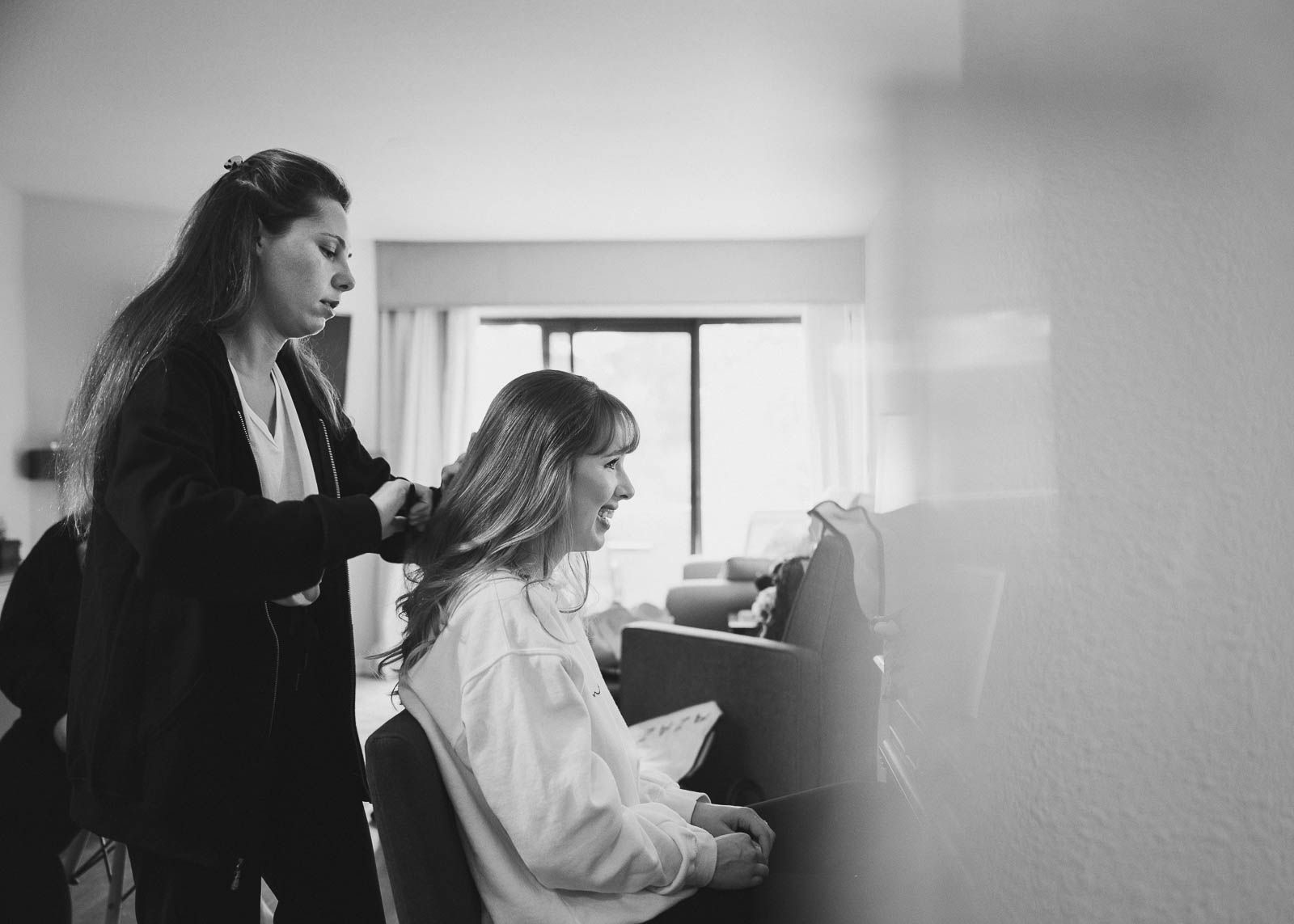 Black and white image of bride having her hair done by friend
