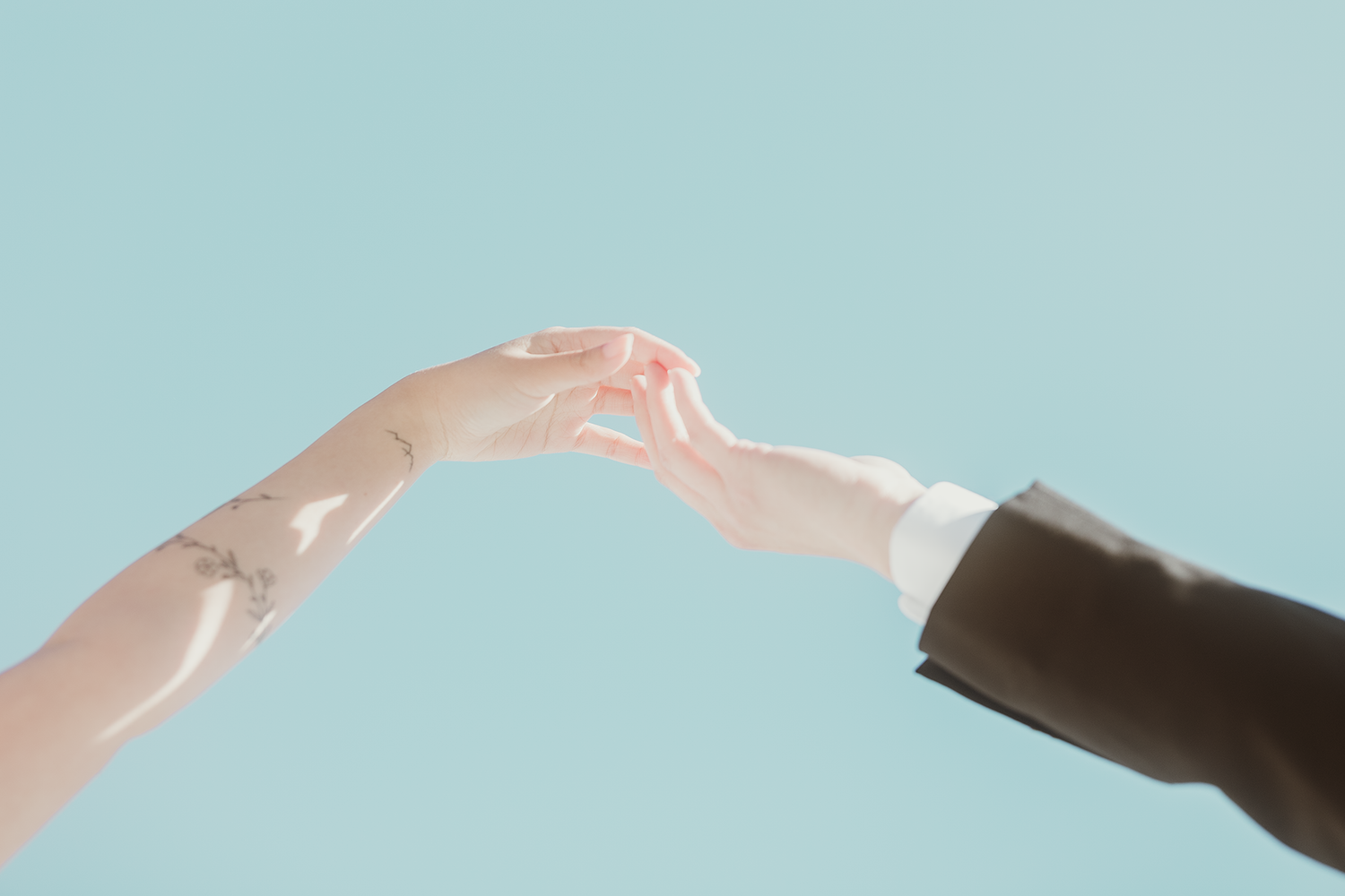 Two hands reaching towards each other against a light blue background.