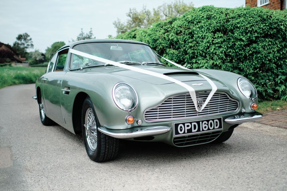 A classic silver Aston Martin DB6 decorated with white ribbons for a wedding.