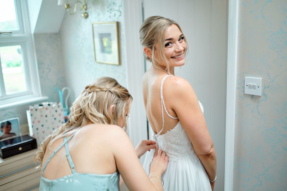 A bridesmaid helps adjust a wedding dress during preparation.