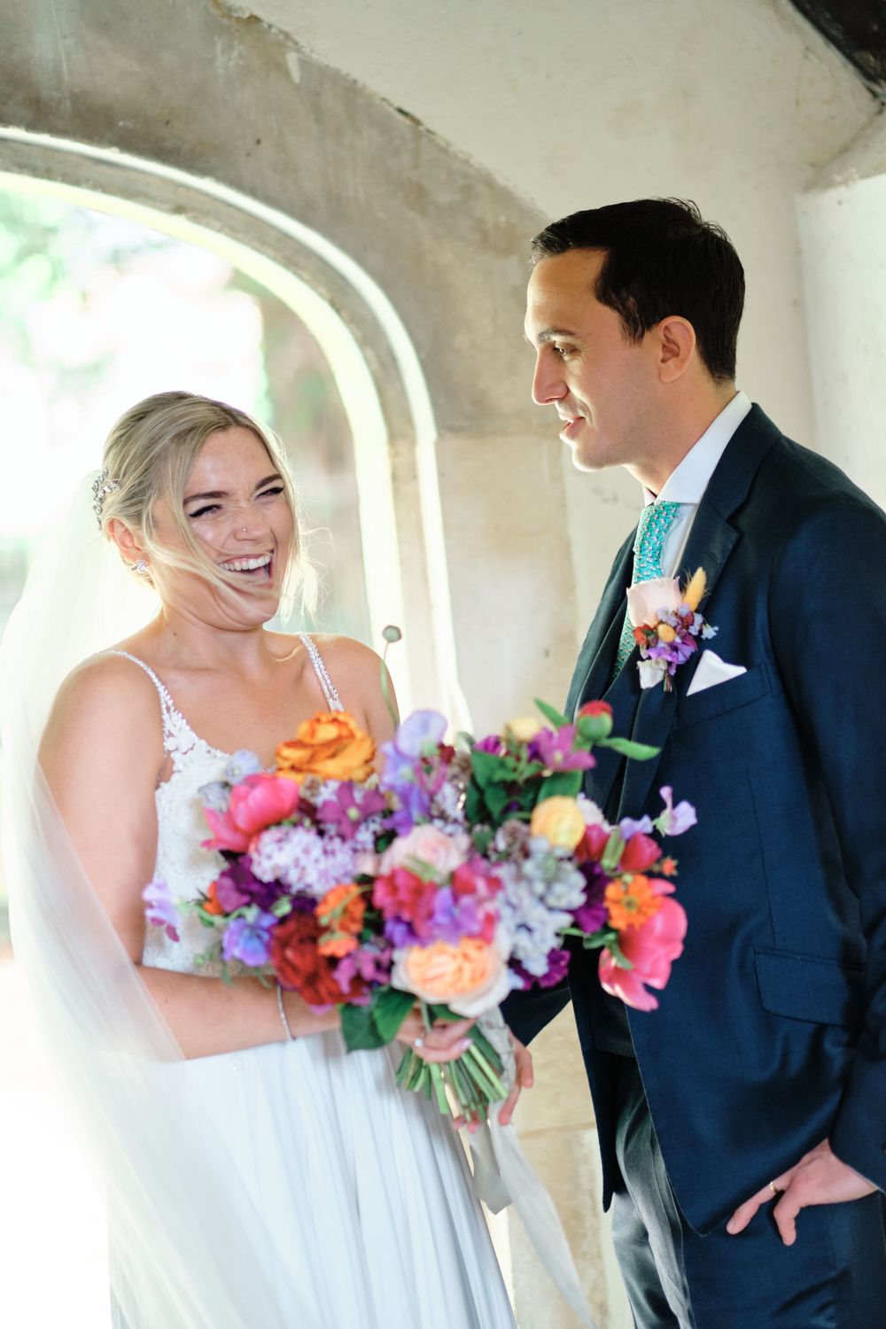 A couple shares a joyful moment with colorful wedding bouquet under an archway.