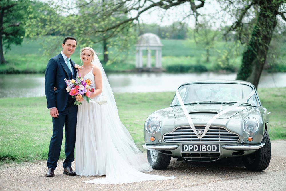 Wedding portrait with classic silver Aston Martin and garden gazebo in the background.