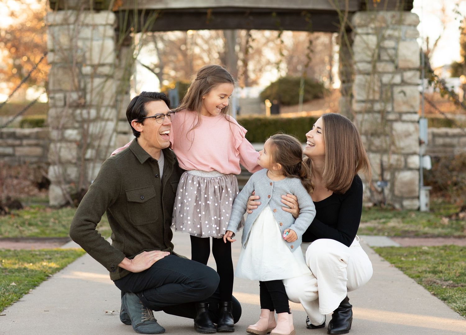 Family portrait under a stone archway in a park setting.
