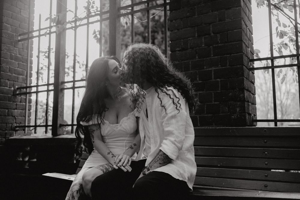 A couple sharing an intimate moment on steps by a brick wall in moody lighting.