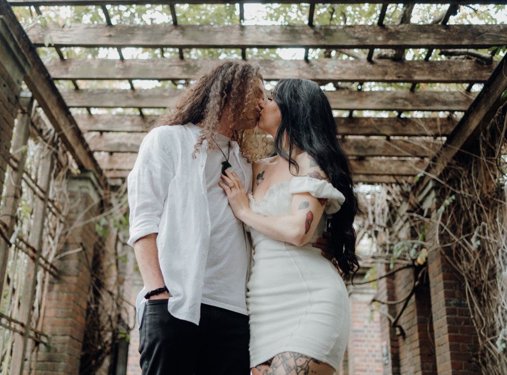 A couple embraces in an intimate moment under a rustic wooden pergola.