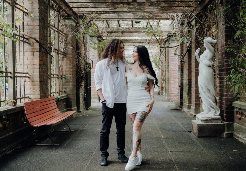 A couple walks together through an ornate covered walkway with classical architecture.