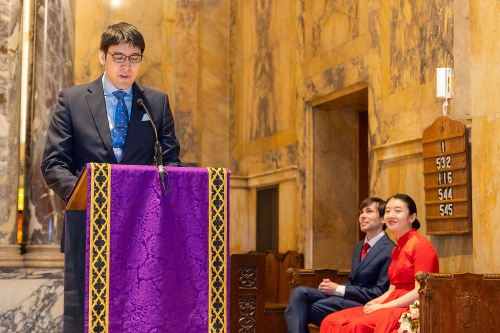 Speaker at church podium with purple draping during formal ceremony.
