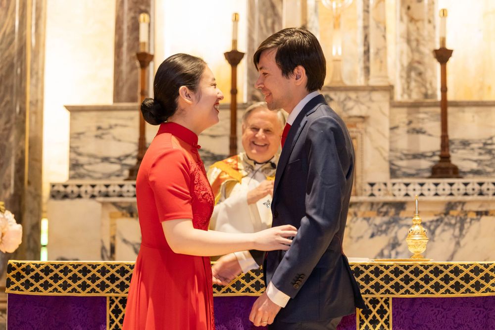 A couple embraces during a wedding ceremony in front of an ornate altar with candles.