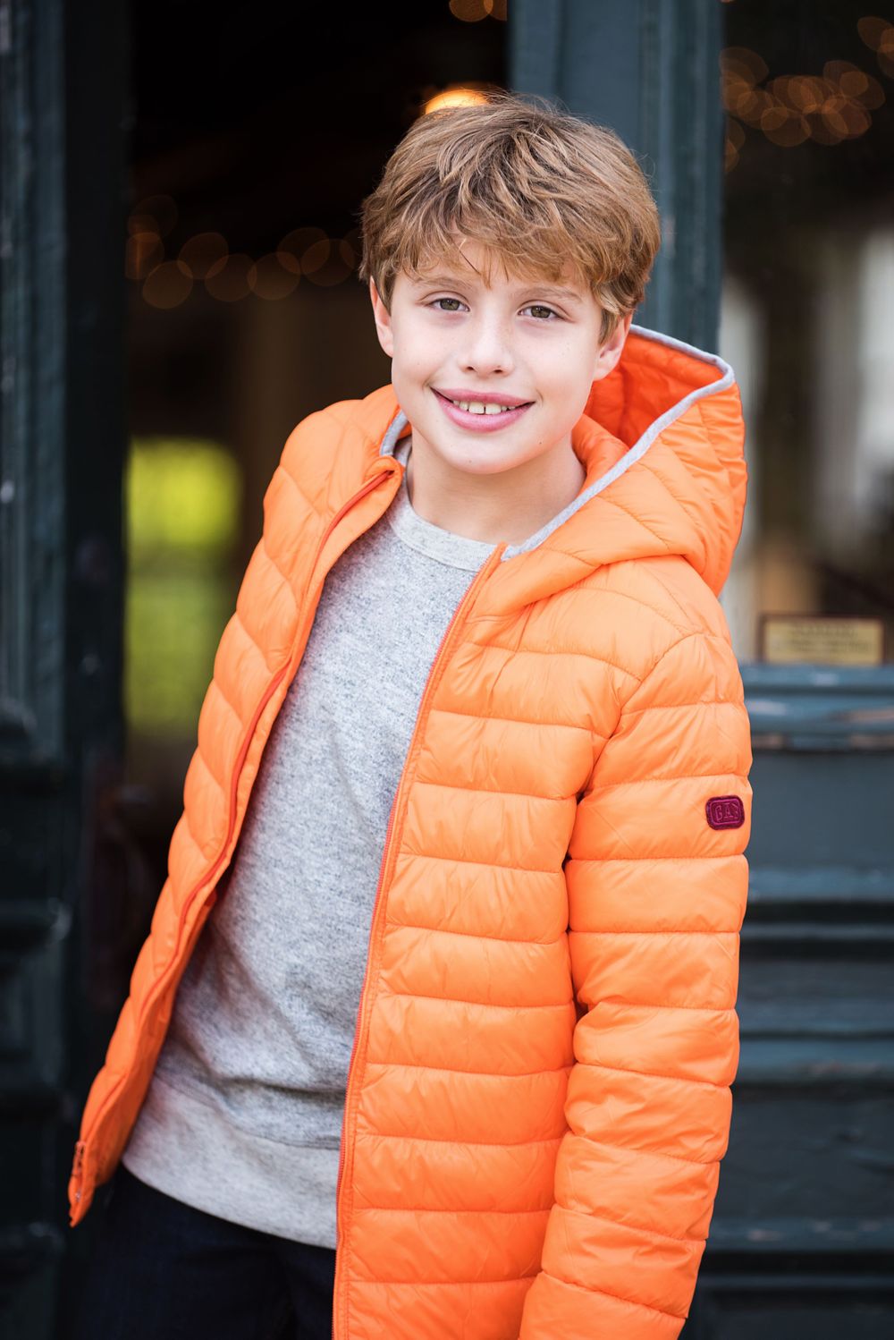 Tween male model wearing orange puffer stepping out of a doorway