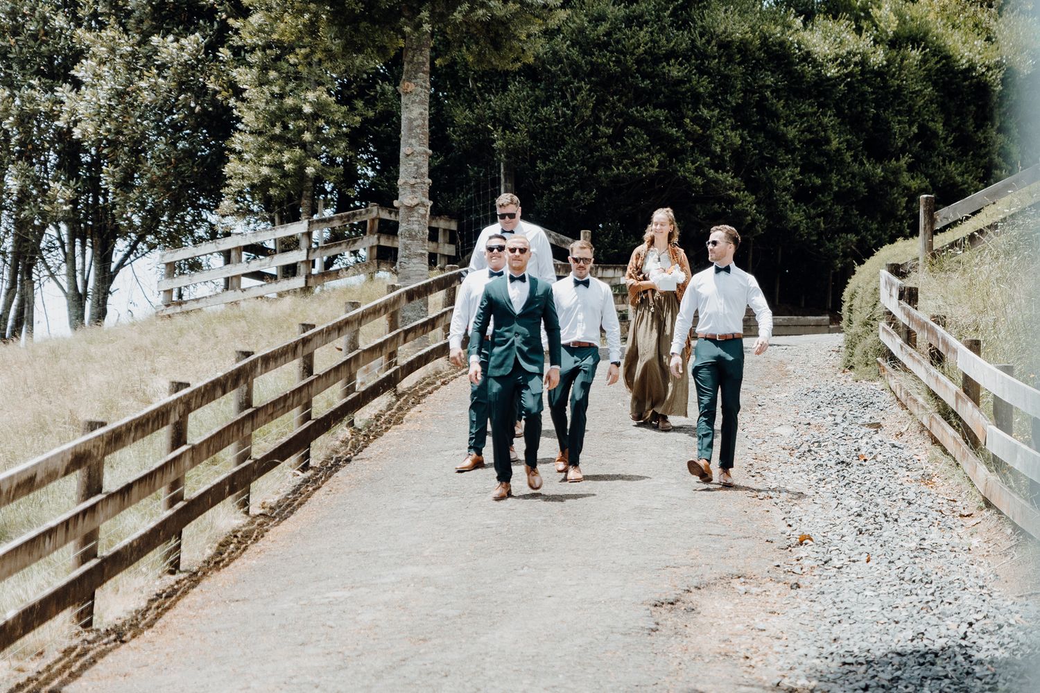 A group walks along a wooden fence-lined path surrounded by greenery.