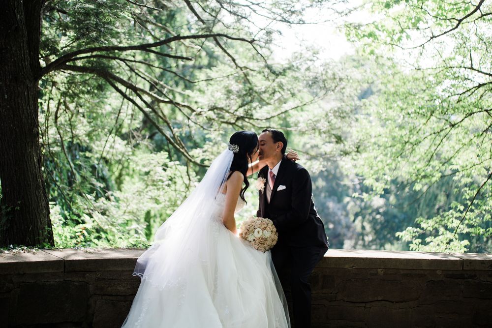 Bride and groom sit on a stone wall and share a kiss