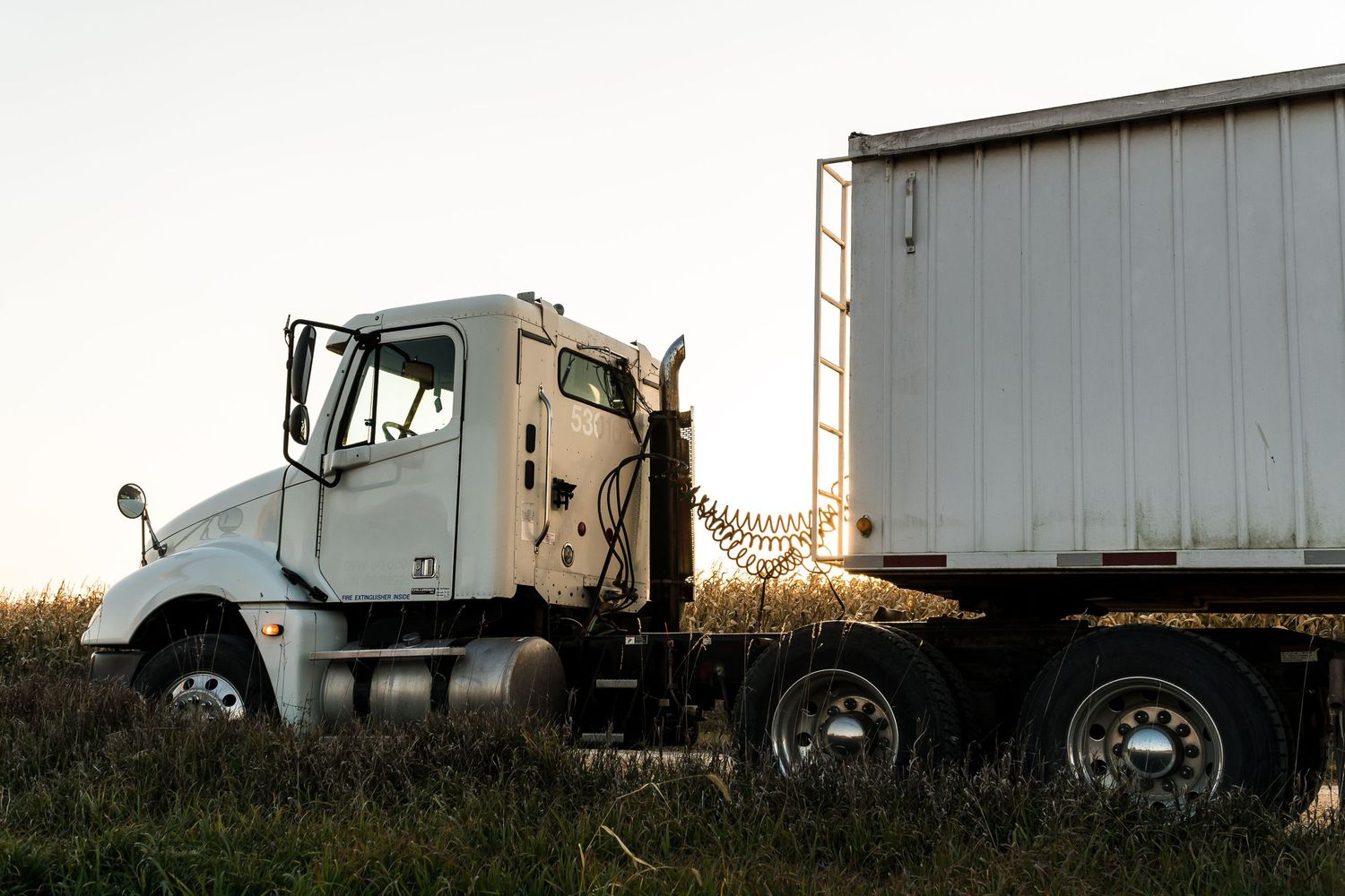 Semi truck with white trailer parked in field during golden hour.