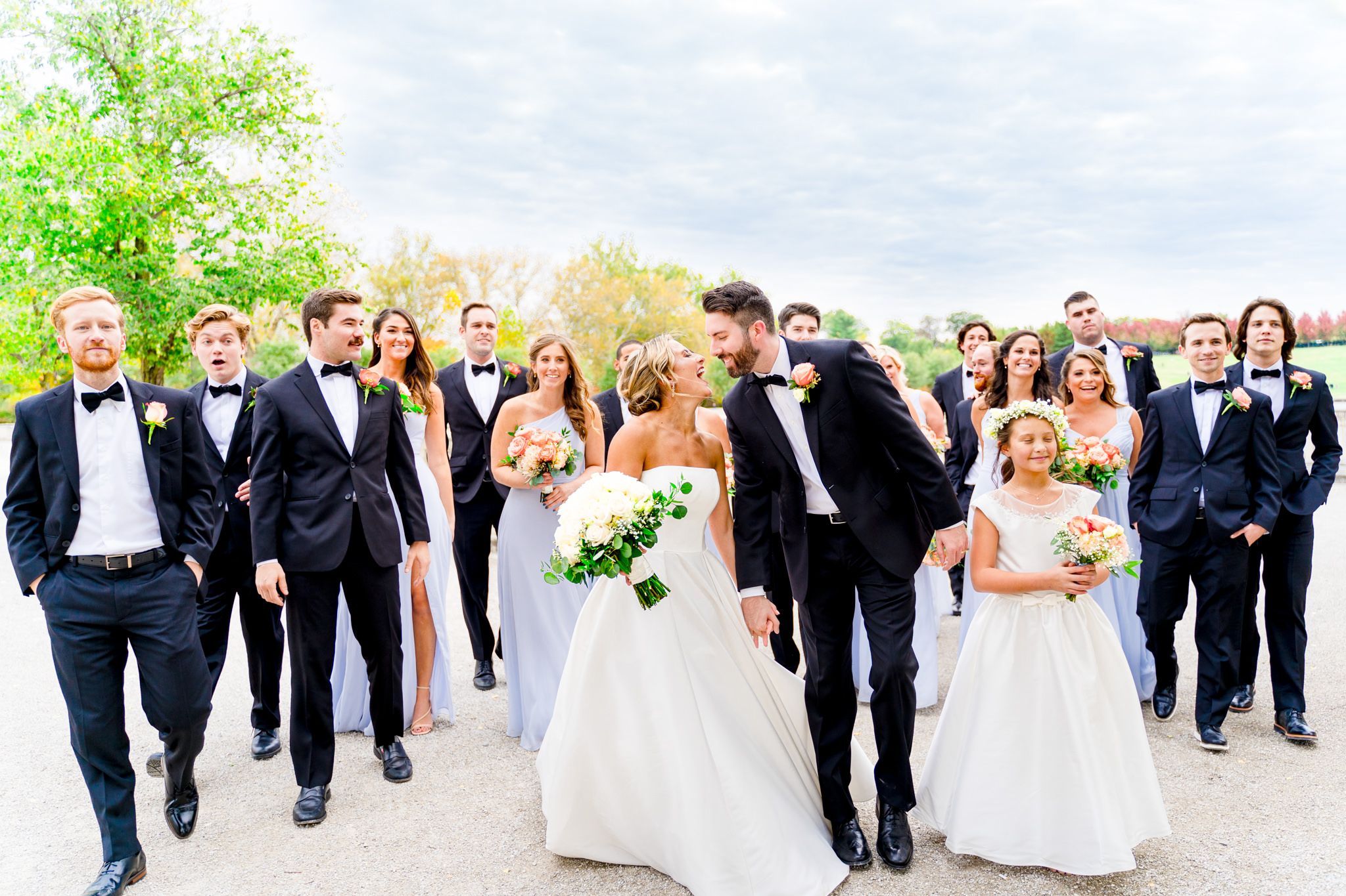 large wedding party in black suits and light blue dresses walk with bride and groom at Forest Park STL fall wedding