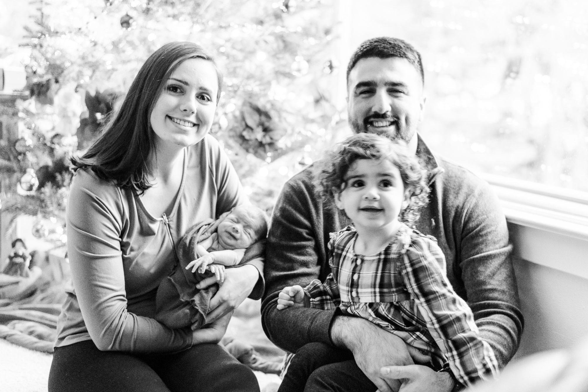 Lifestyle family sitting in front of Christmas tree holding newborn baby in Pittsburgh, Pennsylvania