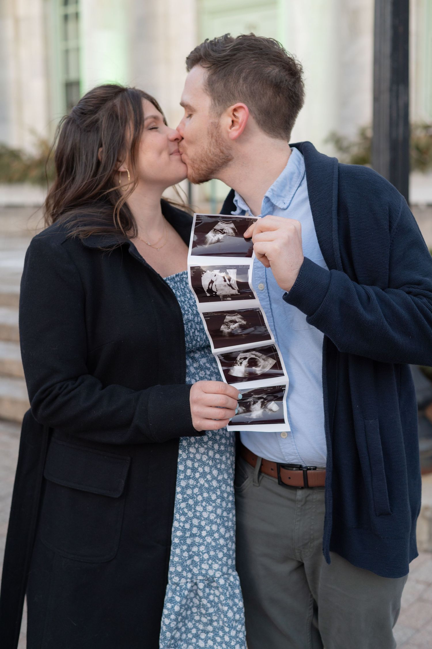 Romantic moment between couple holding ultrasound photos outside.