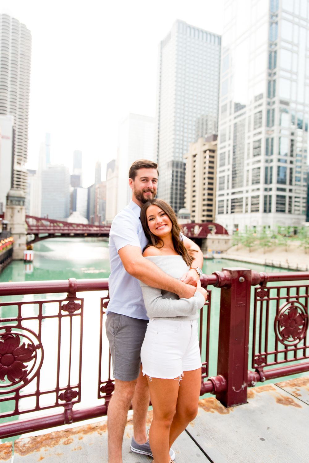 man with brown hair hugging fiance from behind, looking at the Chicago River for sunrise engagement pictures in Chicago