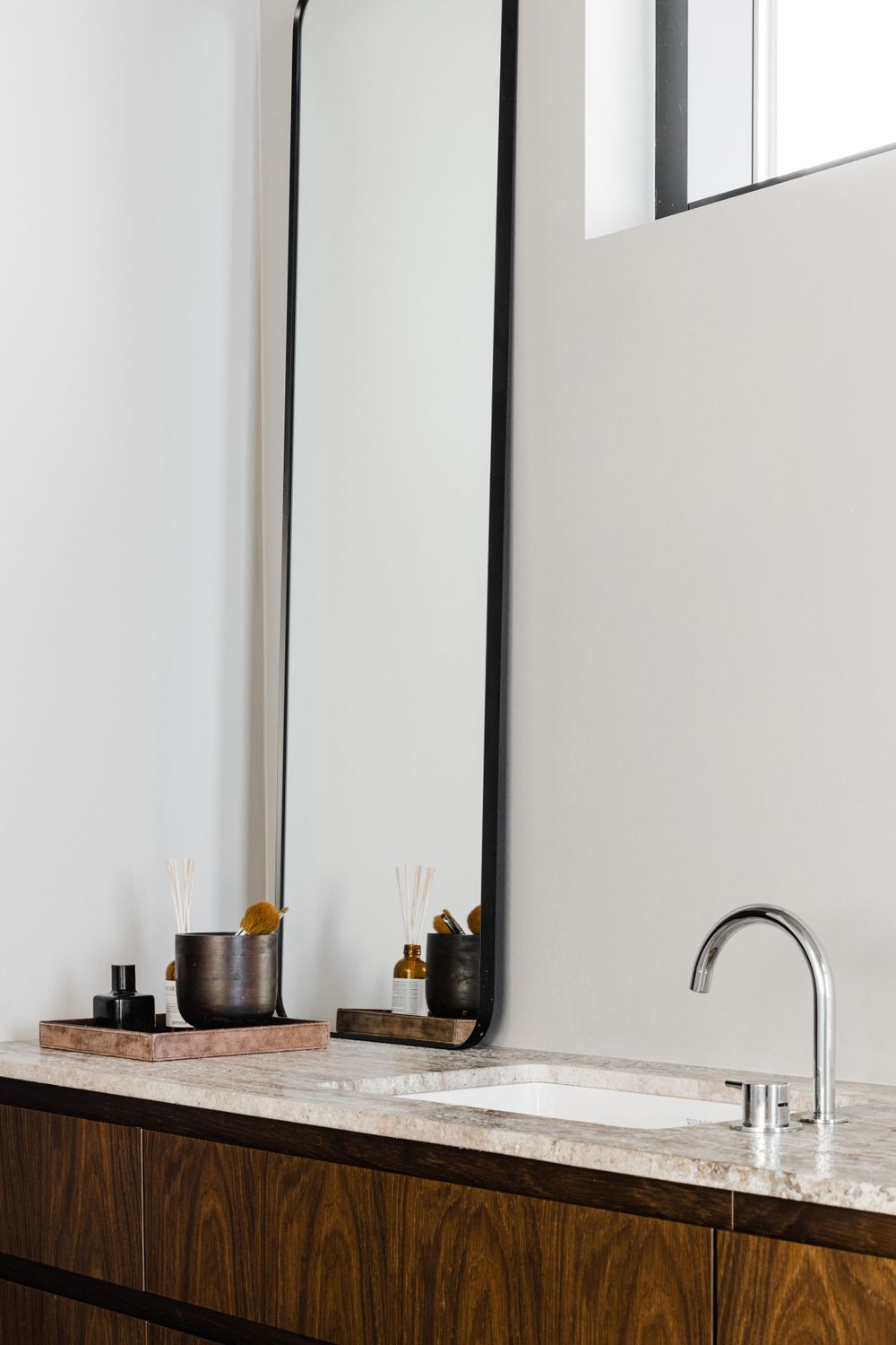 Minimalist bathroom vanity with tall mirror, marble countertop and dark wood cabinetry.