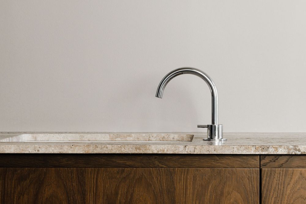 Sleek chrome faucet mounted on marble countertop against wooden cabinet base.