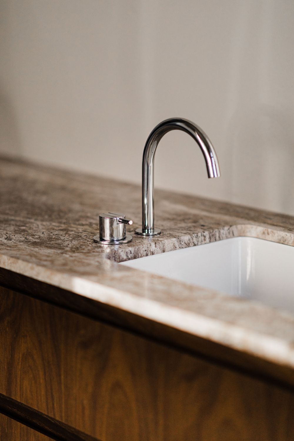 Modern chrome faucet mounted on marble countertop with white undermount sink.