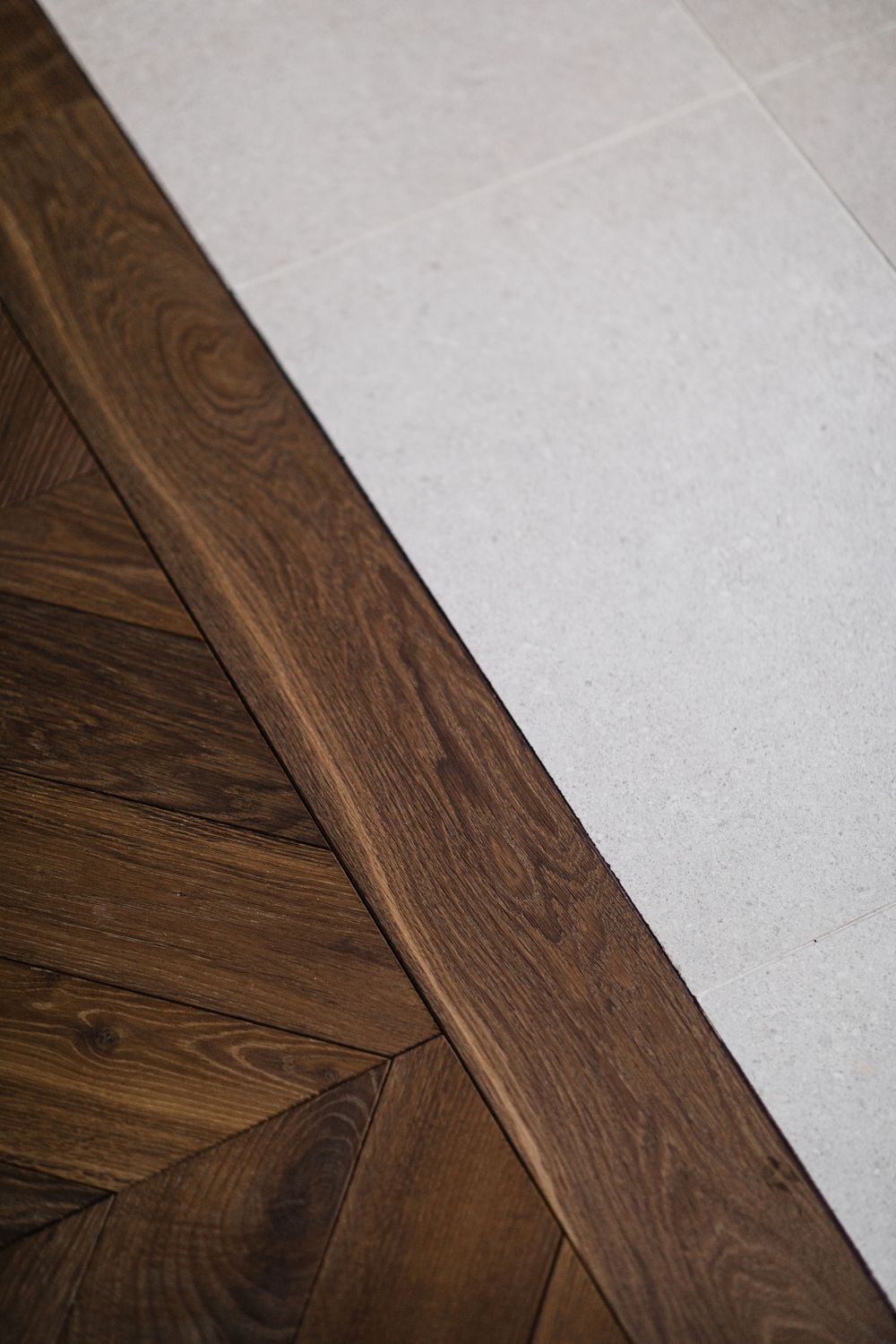Close-up of herringbone wood flooring meeting light colored stone tiles with distinct grain patterns.