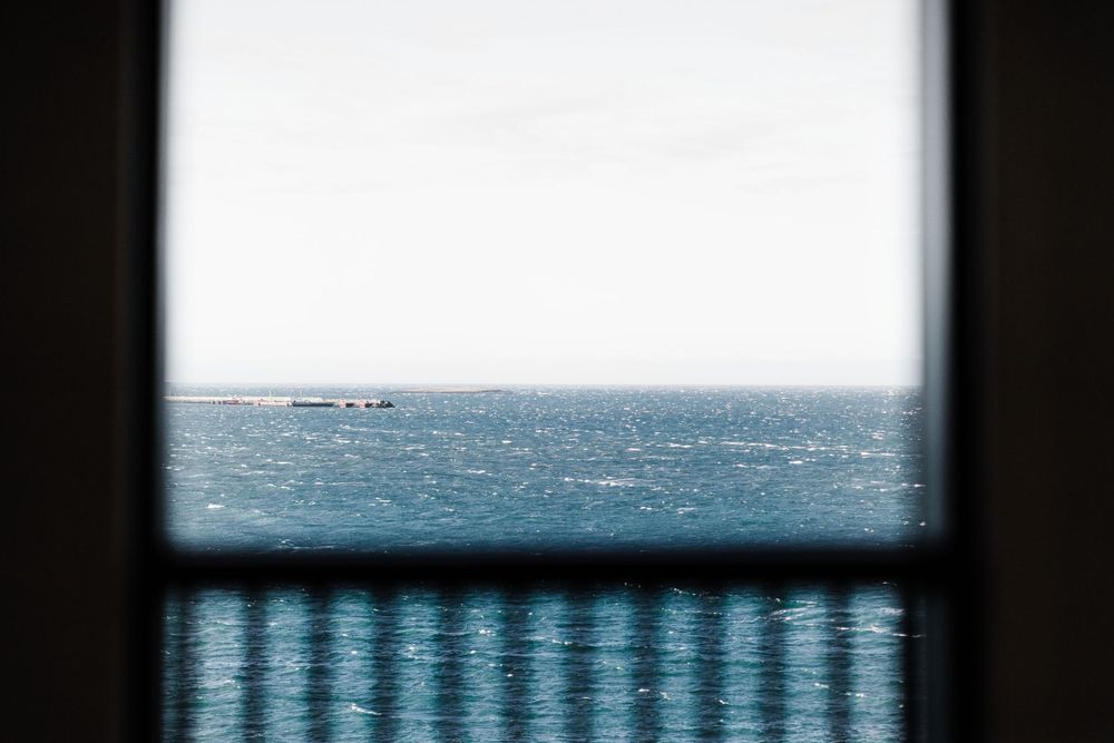 Ocean view through a window frame with sunlight reflecting on rippling water.