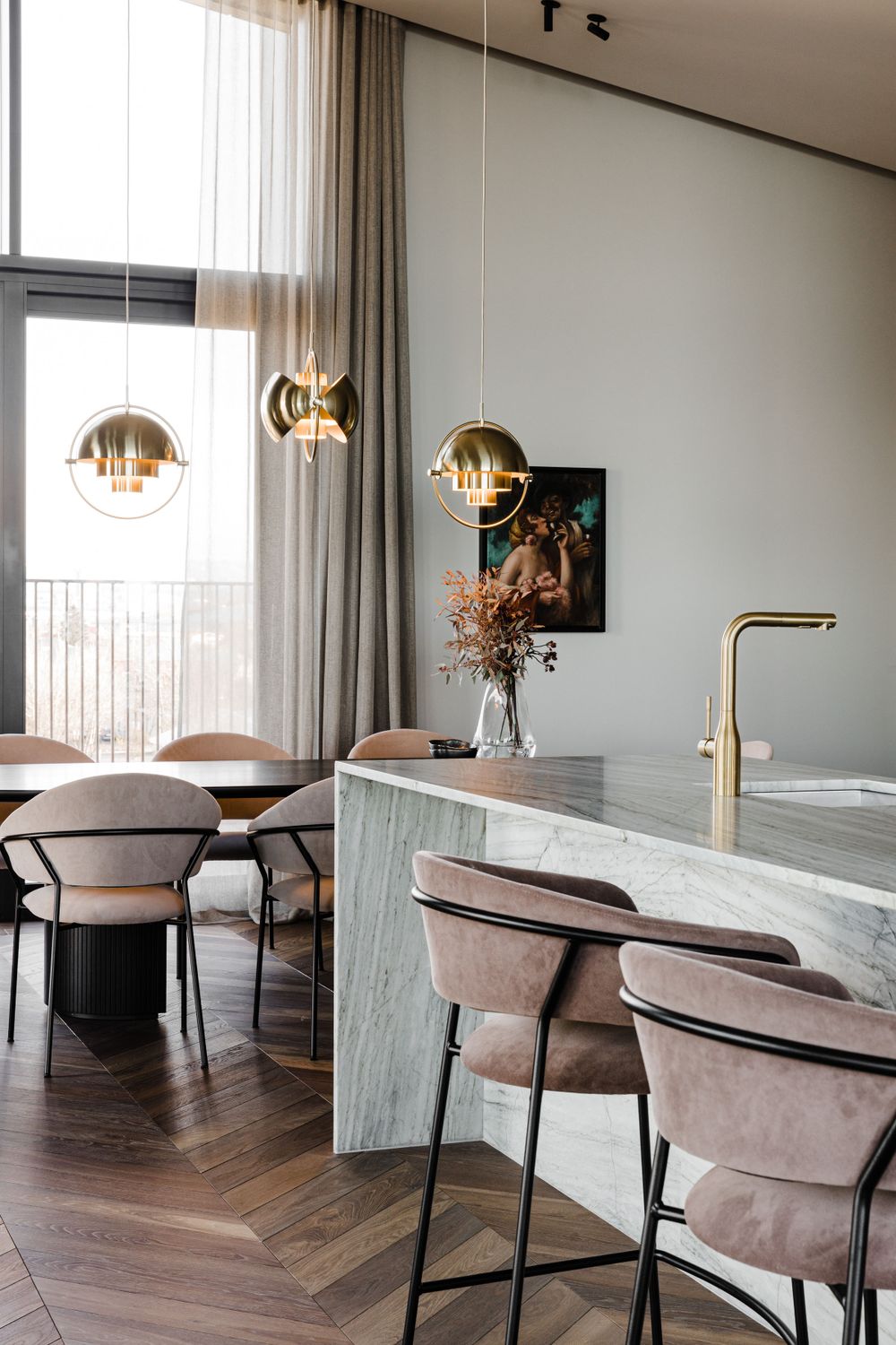 Luxurious dining area with velvet bar stools, marble counter, and gold pendant lights by large windows.