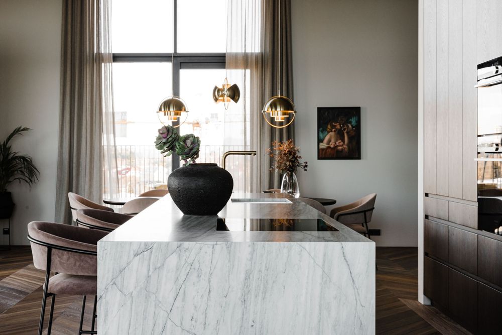 Modern kitchen island with white marble surface, black vase, and gold pendant lights hanging above.