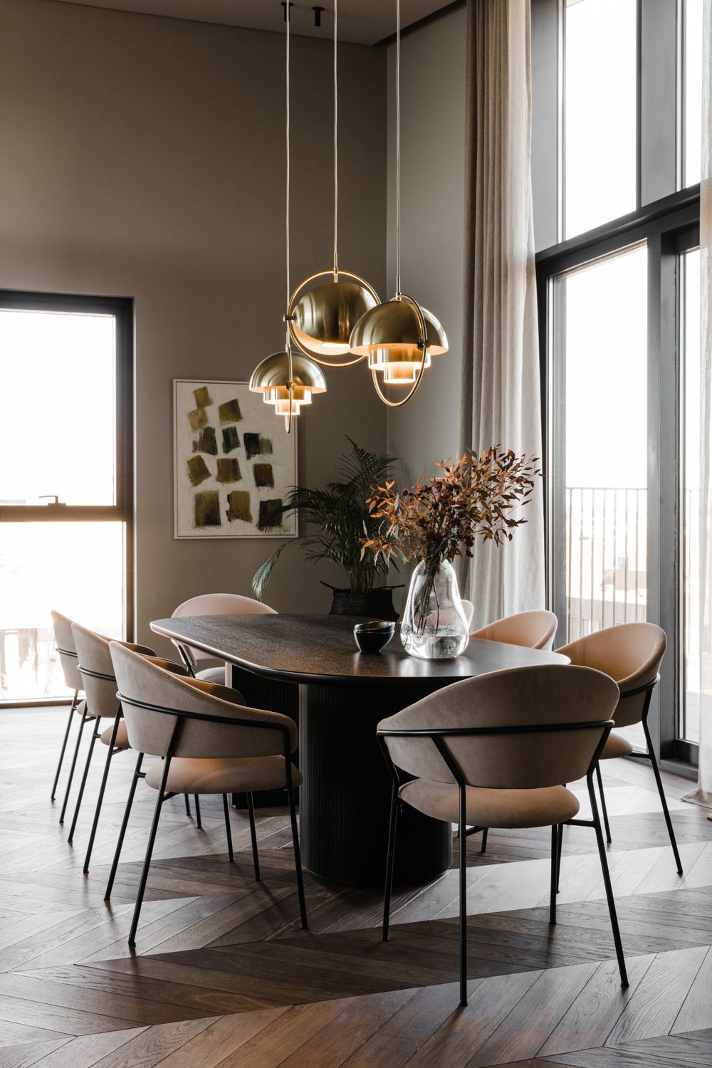 Contemporary dining area with oval table, modernist chairs, and gold pendant lights by floor-to-ceiling windows.