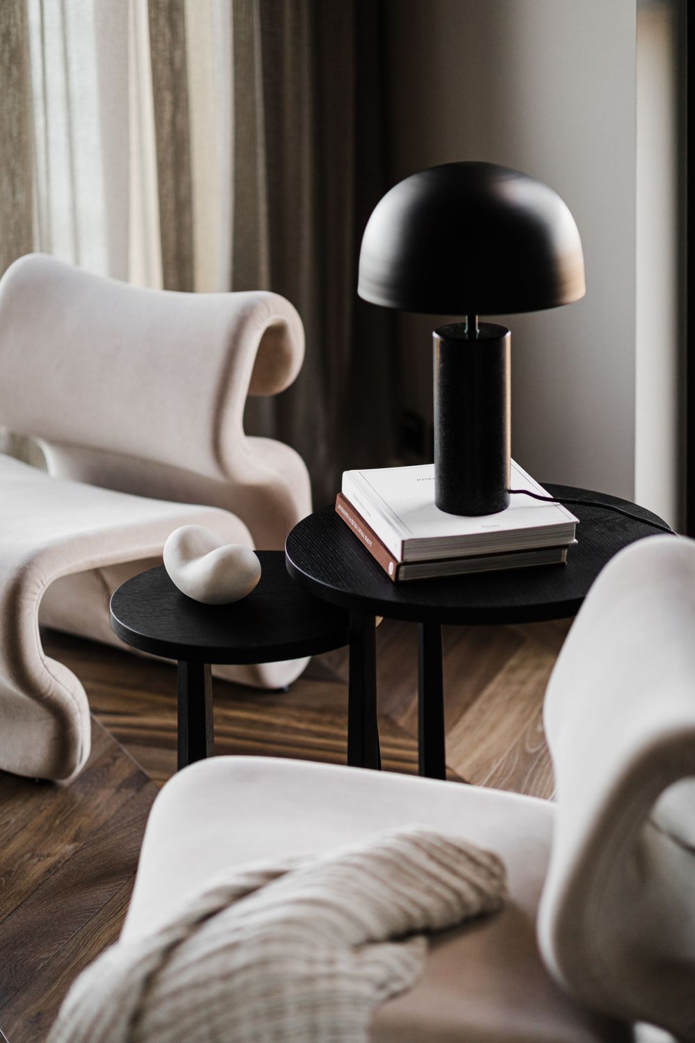 Stylish seating area with white curved chairs, black dome table lamp, and modern accent pieces.