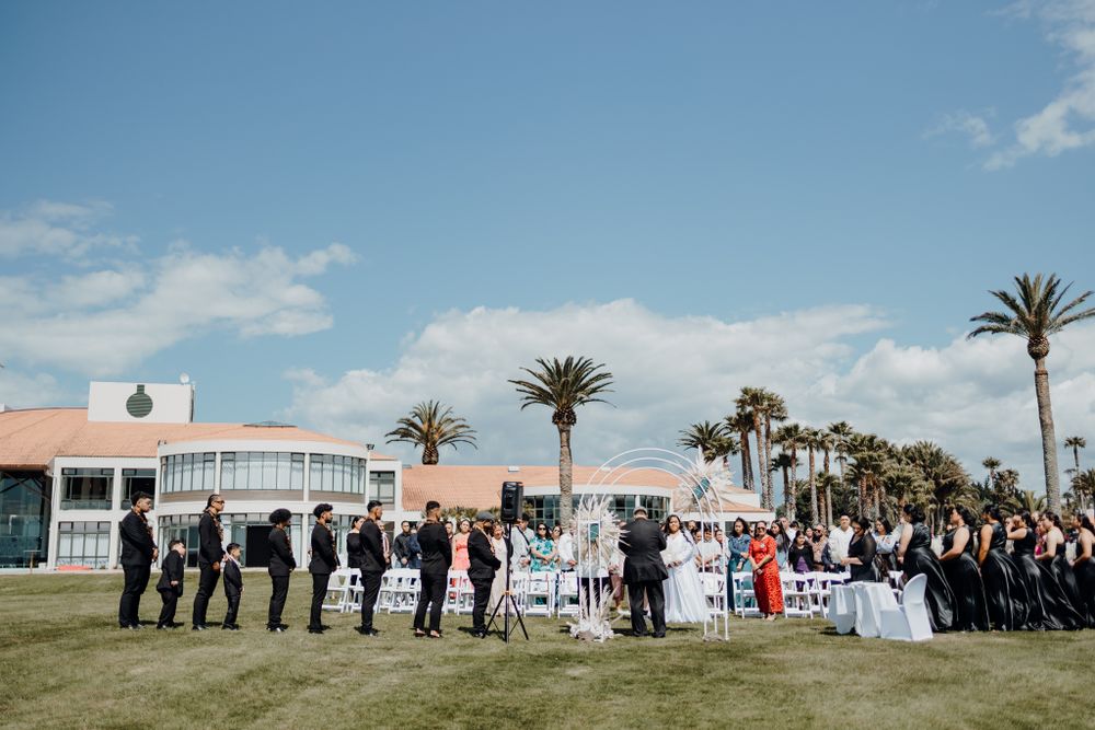 Wide shot of a wedding ceremony setup with white chairs and palm trees against a blue sky.