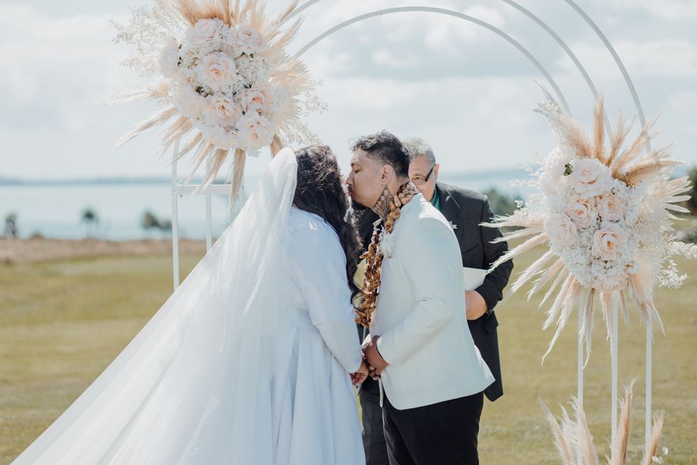 Couple exchanging vows under a decorated arch with pampas grass at their outdoor ceremony.