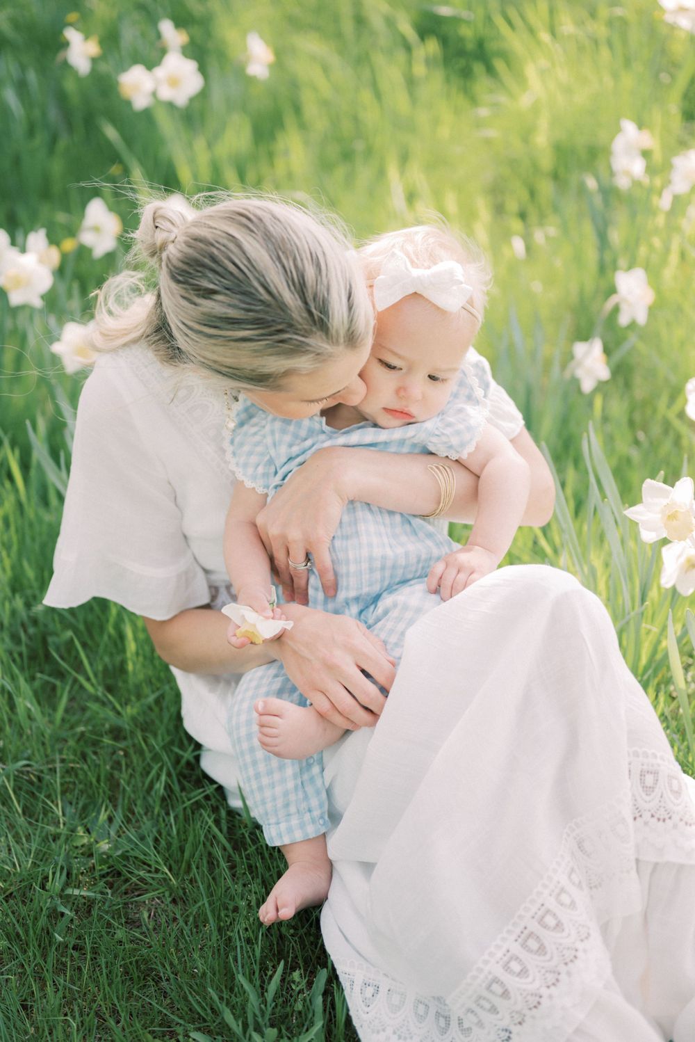 A sweet outdoor portrait in a field of daffodils showing parent and baby in white and blue outfits.