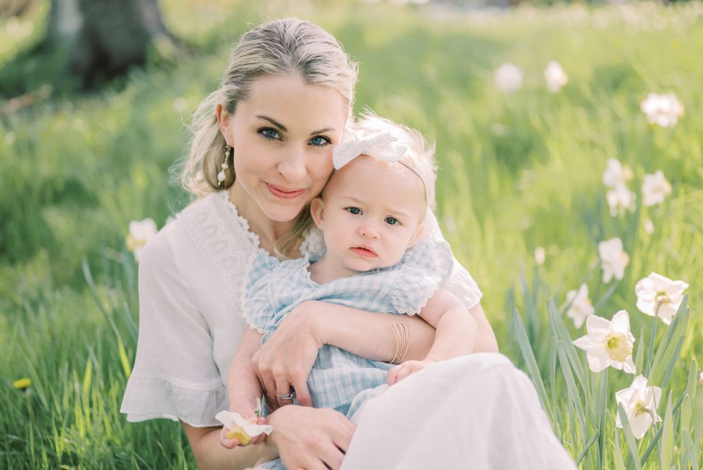Springtime portrait of parent and baby sitting together among blooming daffodils.