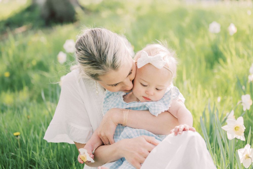 Intimate outdoor moment between parent and baby surrounded by spring flowers.
