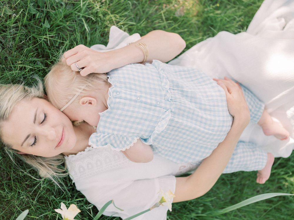 Parent and baby laying in grass together surrounded by white spring flowers.