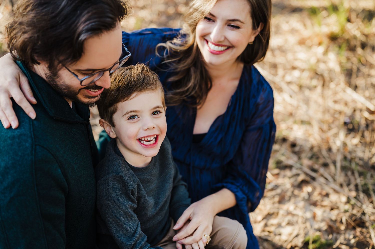 family of three taking family portraits in a park in houston with a child smiling