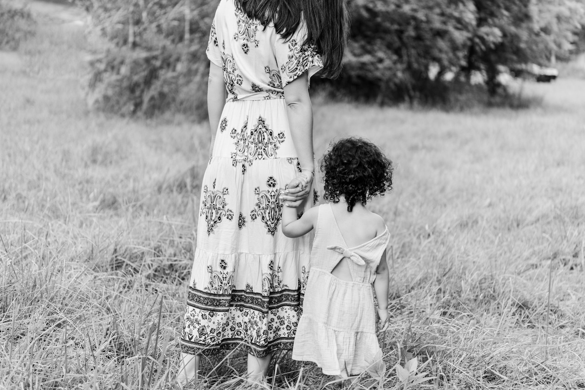 Mother and young daughter walking away through field holding hands in black and white in Pittsburgh, Pennsylvania