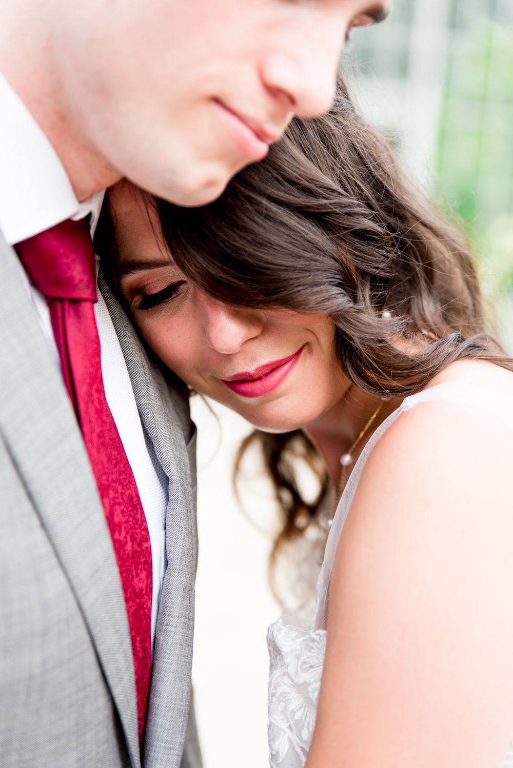 bride smiling with eyes closed while laying on groom's chest in front of Krohn Conservatory in the summer