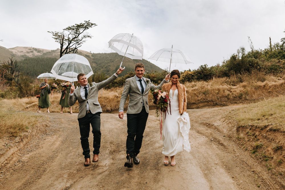 Groom holding umbrella over bride on mud path in North Canterbury