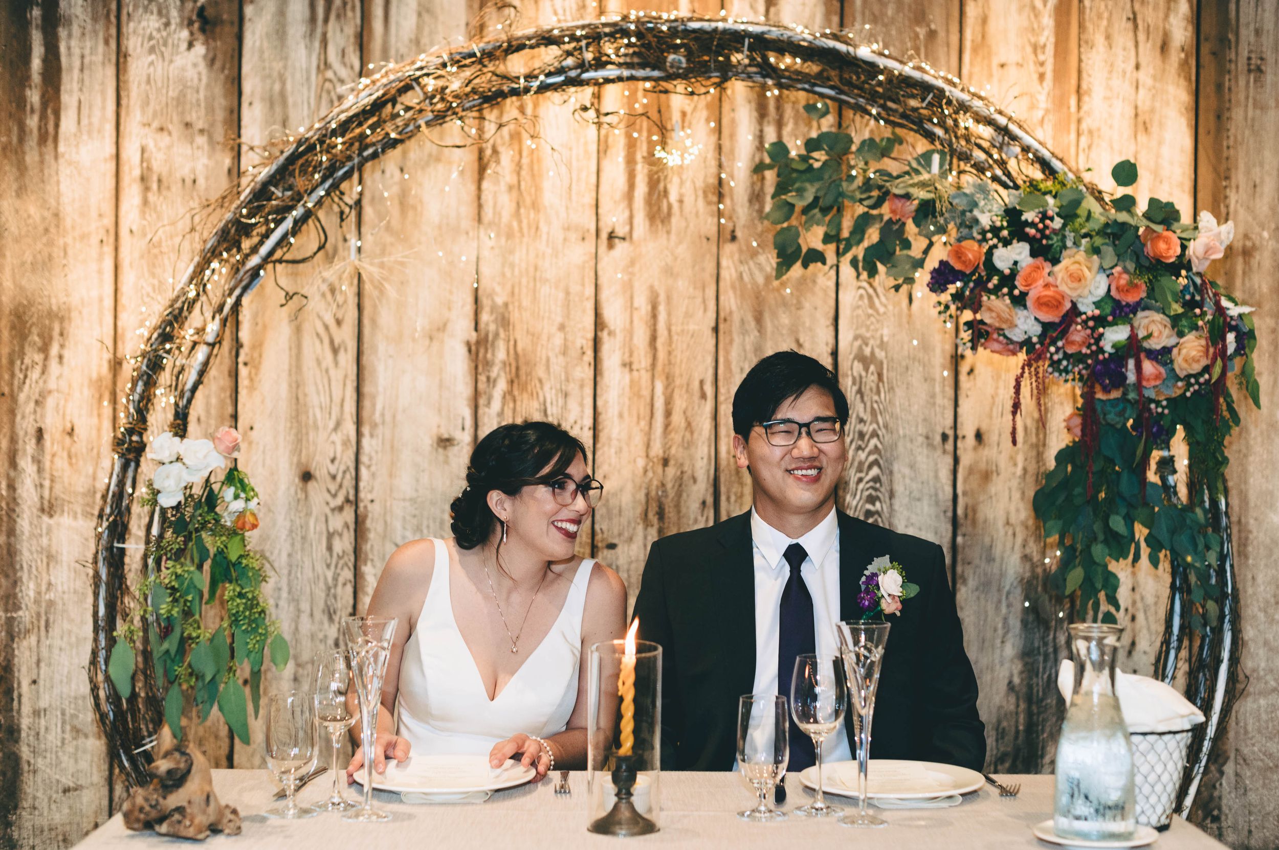 Bride and groom at their sweetheart table in front of the arch used at the ceremony