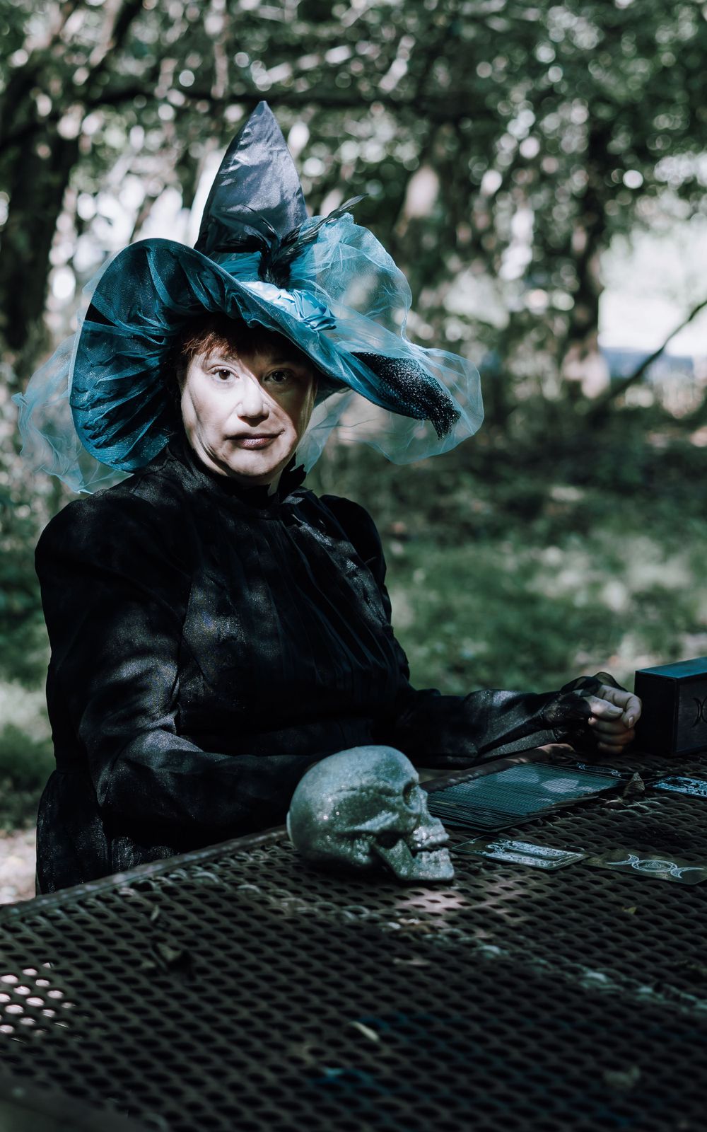 Witch looking towards the camera a skull is beside her and tarot cards are laid out
