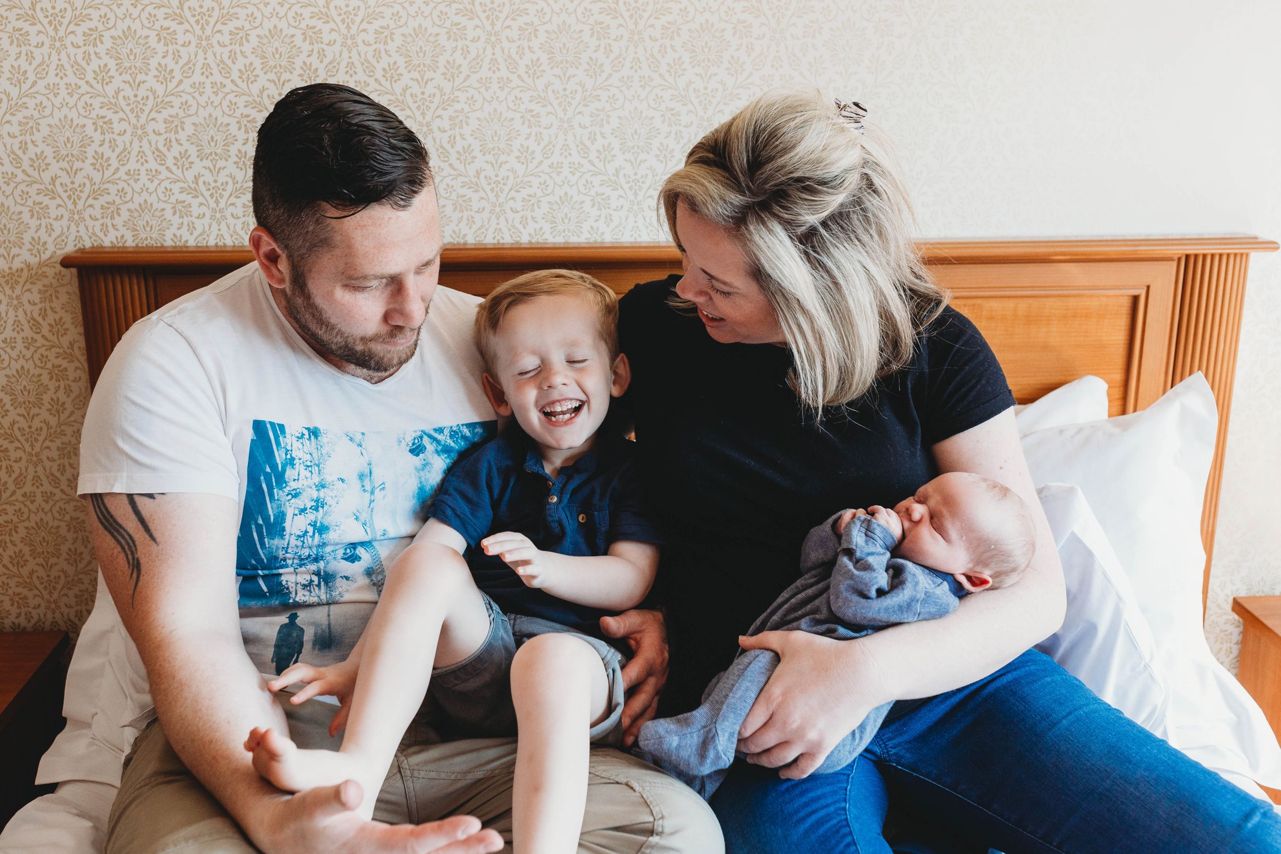 family of four sitting on bed toddler boy laughing