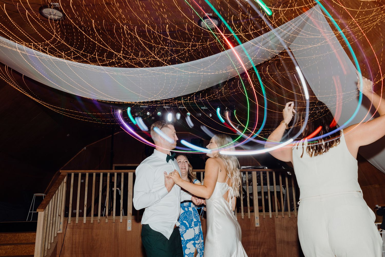 Guests dancing at wedding reception under dramatic LED light installations and white draping.