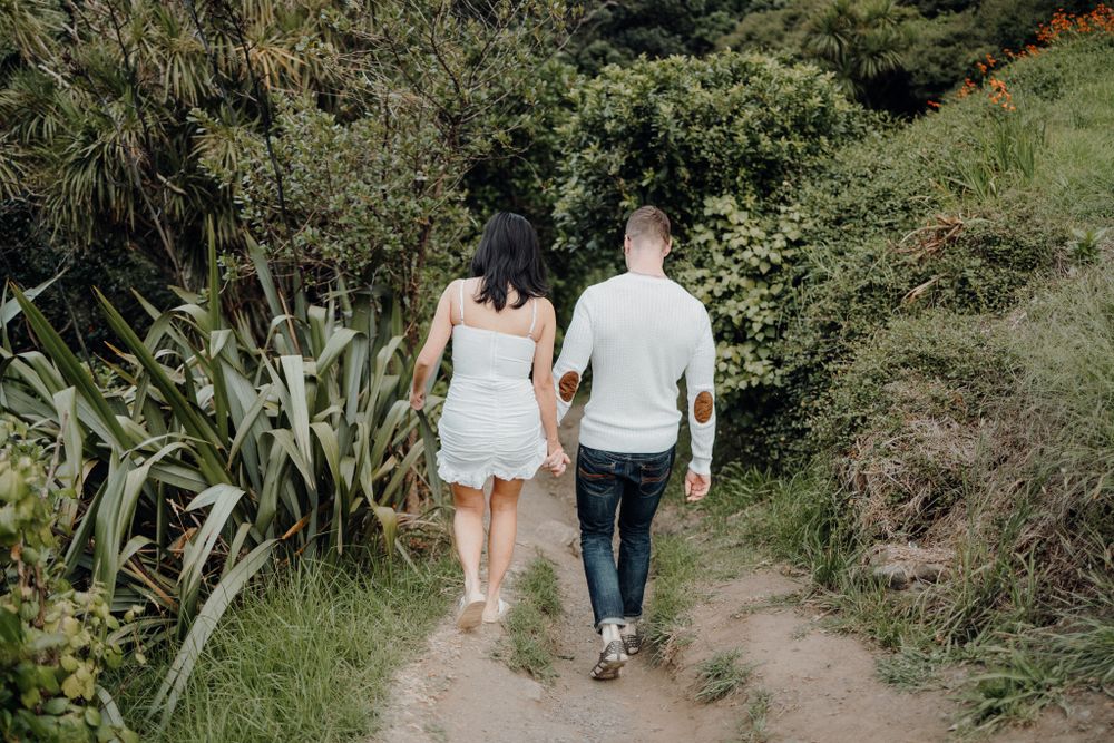 Couple walking hand in hand on nature trail surrounded by lush greenery.